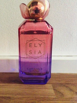 Elysia Elegance parfym  - Elysia Elegance från Fragrance World är en parfym i en snygg glasflaska med rosa till lila färgskiftning och guldfärgat lock. Doften har blommiga, fruktiga och citrusaktiga toner med inslag av päron, mandarin, apelsin och persika.Se bild hur mycket använt 