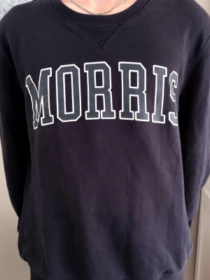 Mörkblå sweatshirt från Morris - Mörkblå sweatshirt från Morris med stor vit logga över bröstet. Andvänt men bra skick.