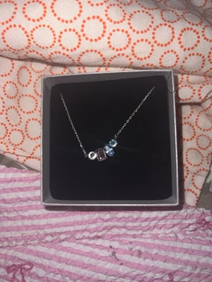 Silverhalsband med färgade pärlor - Snyggt halsband i silverfärgad metall med tre pärlor i olika färger – en ljusblå, en klar och en ljusrosa. Pärlorna har olika former och ger halsbandet en modern och stilren look. Perfekt accessoar för att lyfta din outfit.