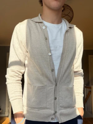 Stenströms Cardigan – Beige – Strl S - Säljer en stilren och mycket användbar cardigan från Stenströms i en elegant ljusbeige färg. Perfekt att bära över t-shirt eller skjorta för en välklädd och tidlös look.  Märke: Stenströms Storlek: S Färg: Ljusbeige / Sand Skick: Mycket fint skick  • Klassisk knappstängning • Två framfickor • Mjuk och bekväm kvalitet • Passar lika bra till vardag som till mer uppklädda tillfällen • Tidlös modell som aldrig går ur stil