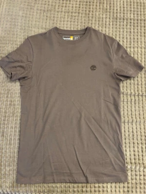 Brun t-shirt från Timberland - Snygg brun t-shirt från Timberland med diskret logga på bröstet. Klassisk rund halsringning och korta ärmar. Tillverkad i mjuk bomull för skön känsla och enkel stil. Perfekt basplagg till garderoben.