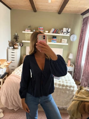 Mörkblå v-ringad blus med puffärm - Så fin blus nu till sommaren! Den har knäppning vid bysten och sedan öppen slits. Tyvärr har den översta knappens spänne töjts ut, fastän jag ej använt den så mycket, då den är lite för liten för mig!💖Annars är den i fint skick! Slutsåld.