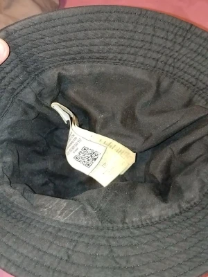 Svart bucket hat från Stone Island - Säljer en svart bucket hat från Stone Island med klassisk logopatch framtill. Hatten är tillverkad i ett slitstarkt tyg och har en bred, nedåtlutande brätte. Perfekt accessoar för en streetwear-look.