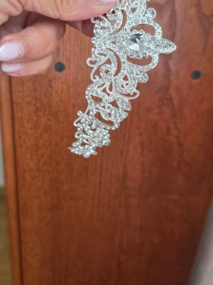 Glittrigt diadem med strassdetaljer - Snyggt diadem i silverfärgad metall med massor av glittrande strass och en stor kristall i mitten. Diademet har ett elegant, utskuret mönster som ger en lyxig känsla och passar perfekt när du vill sticka ut lite extra.
