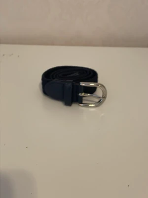 Svart bälte med silverfärgat spänne - Snyggt svart bälte med ett stilrent silverfärgat spänne. Bältet har en klassisk design och passar perfekt till jeans eller byxor. Materialet ser ut att vara skinn eller syntet och bältet är smalt vilket ger en clean look.