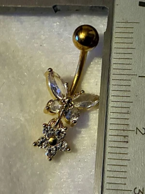 NY oanvänd Navelpiercing med hänge | Kirurgiskt stål | Fjäril, blomma och vita stenar  - 💕30% Bundle-rabatt vid köp av minst 2 artiklar. ⭐️NY oanvänd piercing i kirurgiskt stål; rostfritt och säkert för läkta piercingar.                               📏MÅTT ⭕️Stavens längd: 10mm ⭕️Stavens tjocklek: 1,6mm  ⭕️Smyckets totala längd: 25mm                                                                          🤍Färger: Guld och vit                                                             💌Skickas spårbart via Plick SafePay.