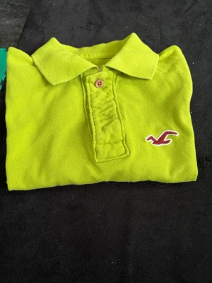 Limegrön Hollister pikétröja S - Säljer en limegrön pikétröja från Hollister med klassisk krage och knappslå. Tröjan har korta ärmar och är tillverkad i mjuk bomull. Hollisters logga är broderad på bröstet. Perfekt för dig som gillar färgstarka plagg!