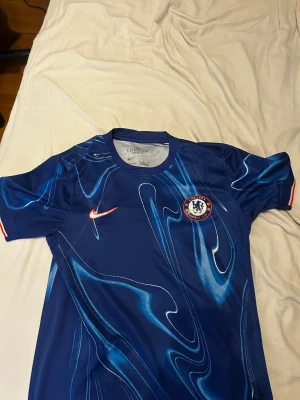 Chelsea FC blå matchtröja Nike - Chelsea FC matchtröja i blått med  mönster i ljusblått och vitt. Tröjan har klubbmärke och Nike-logga på bröstet samt korta ärmar. Perfekt för fotboll eller träning.