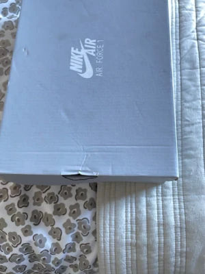 Nike Air Force 1 vita sneakers - Klassiska vita Nike Air Force 1 sneakers i lågt utförande. Skorna är helvita med den ikoniska swoosh-loggan på sidan och har en chunky sula. Tillverkade i läder med perforerade detaljer på tån för extra ventilation. Perfekta för en clean och stilren look.