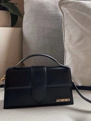 Svart  handväska i faux skinn - Säljer en svart handväska i slätt faux skinn med guldfärgad logga. Väskan har ett stilrent, rektangulärt format och både handtag och axelrem för olika sätt att bära. Dustbag ingår (ej prislapp!!)☀️