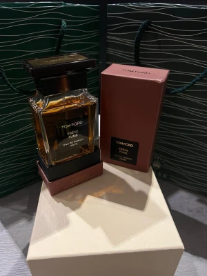 Tom Ford Ébène Fumé Eau de Parfum - Tom Ford Ébène Fumé Eau de Parfum 100 ml kommer i en elegant, fyrkantig glasflaska med mörkbrunt lock och detaljer. Doften presenteras i en stilren brun kartong med svart etikett. Flaskan har en lyxig och modern känsla, perfekt för dig som gillar exklusiva parfymer.