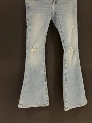 Jeans Gina 14 + - Säljer ett par ljusblå bootcut jeans med slitna detaljer på framsidan. Jeansen har utsvängda ben och klassisk femficksdesign. Perfekta för dig som gillar en retro och avslappnad stil. Materialet är denim i bomull. Ifrån gina 14+ storlek S, använda max 1 gång så i ny skick ❣️