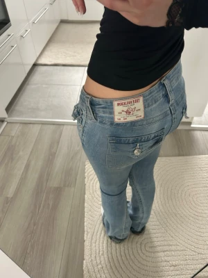 Ljusblå True Religion jeans bootcut - Säljer ett par ljusblå jeans från True Religion med bootcut-modell och låg midja. Jeansen har klassiska sömmar, silverfärgade knappar och ficklock bak med knappdetalj💕