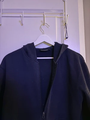 Marinblå hoodie med dragkedja - En enkel marinblå hoodie med dragkedja framtill och huva. Tillverkad i mjukt bomullsmaterial som känns skönt mot huden. Perfekt för chill dagar eller när du vill ha en clean och avslappnad look.