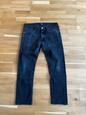 Svarta raka jeans från Lee - Snygga svarta jeans från Lee med klassisk femficksmodell och raka ben. Jeansen har en diskret tvättad look och detaljer i silverfärgad metall. Tillverkade i ett slitstarkt denimtyg som passar perfekt till din vardagsstil. Storlek W31 L32