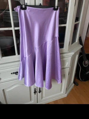 Ljuslila satin långkjol - Säljer en ljuslila långkjol i satin material med volang nedtill. Kjolen har en diskret dragkedja i sidan för enkel påklädning och en snygg, flowy passform. Perfekt för dig som vill sticka ut med en färgglad och trendig look. Har några skavanker (se bilder). Annars bra skick.