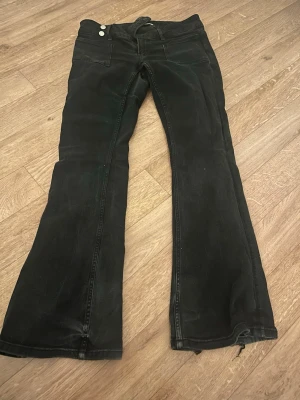 Svarta bootcut jeans med strass, går att pruta priset💕 - Säljer ett par svarta bootcut jeans med två knappar fram och snygga strassdetaljer på bakfickorna. Jeansen har utsvängda ben och klassisk femficksmodell. Perfekta för dig som gillar lite extra bling på dina jeans! Dock så är de lite slitna och därför kan man pruta priset lite gran om man vill💕