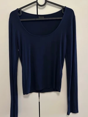 Mörkblå långärmad topp med slits - Mörkblå långärmad topp med rundad urringning och slitsdetalj vid ärmsluten. Tunn och mjuk kvalitet som sitter snyggt på kroppen. Soft touch från ginatricot