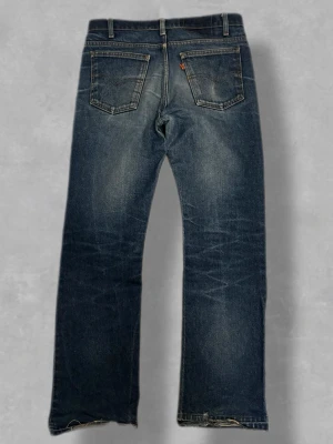 Rare Levis Orange Tabs Vintage W31 - Riktigt feta vintage Levi’s Orange Tab med en fantastisk mörkblå tvätt. Dessa har den perfekta "faden" och naturlig whiskering på låren som bara äkta vintage kan få. Orange Tab tillverkades för att vara mer trendiga och har ofta en snyggare siluett än den vanliga Red Tab-serien. Modellen har en klassisk rak till lätt utsvängd passform (Straight/Bootcut) som sitter riktigt snyggt över sneakers eller boots. • Skick: Mycket gott vintageskick. Karaktärsfullt slitage vid hälarna/bensluten (se bild 5)