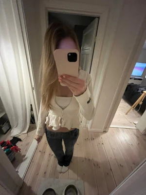 Vit volangkofta från Polo Ralph Lauren - Supersöt vit kofta från Polo Ralph Lauren med dragkedja framtill och dubbla volangdetaljer nedtill. Långärmad och figurnära modell som ger en feminin look. 