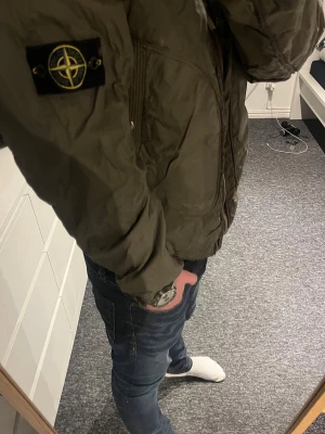 Stone Island grön vindjacka med huva - Snygg grön vindjacka från Stone Island med ikonisk patch på ärmen. Jackan har huva, två stora fickor med knappstängning och dragkedja framtill. Materialet är lätt och syntetiskt, perfekt för blåsiga dagar. Passformen är normal och jackan har långa ärmar. Kontakta gärna mig innan köp!📩