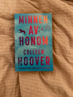 Minnen av honom av Colleen Hoover - En roman med blått omslag och rosa text, skriven av Colleen Hoover. Boken heter 'Minnen av honom' och har motiv av fåglar mot en himmel. Perfekt för dig som gillar gripande och känslosam skönlitteratur.