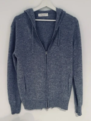 Grå Kashmir zip-hoodie från sayless  - Mysig grå hoodie från Soft Goat i mjuk och lyxig kashmirblandning. Tröjan har dragkedja framtill, två fickor och justerbar huva med snören. 