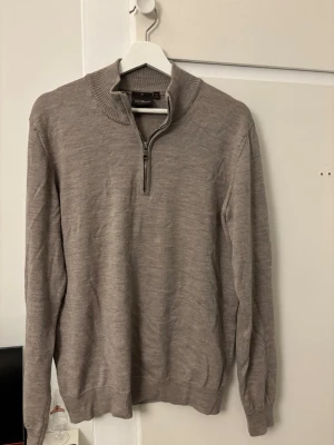 stickad tröja från Oscar Jacobson - Säljer en beige stickad tröja från Oscar Jacobson, tillverkad i Italien. Tröjan har en halvzip med ribbad krage och muddar vid ärmslut och nederkant. Perfekt för lager-på-lager och snygg till jeans eller chinos.