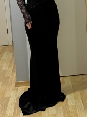 Svart långklänning med spetsärmar - Elegant svart långklänning med figurnära passform och långa spetsärmar. Klänningen har vackra detaljer i spets upptill och en lätt släp nedtill. Perfekt för en extra speciell kväll. Storleken är Tysklands 38 men passar 36/38 