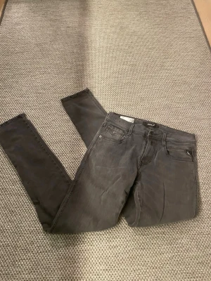 Grå skinny jeans från Replay - Säljer ett par gråa skinny jeans från Replay med klassisk femficksdesign och dragkedjegylf. Jeansen har en snygg tvättad look och är tillverkade i stretchigt material för skön passform. Perfekta till en avslappnad stil.