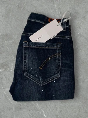 Mörkblå jeans från Dondup | Helt nya! - Säljer ett par mörkblå jeans från Dondup med raka ben och slitna detaljer samt vita färgstänk. Jeansen har klassisk femficksmodell och kontrastsömmar. Perfekta för en avslappnad och trendig look. Modell: George
