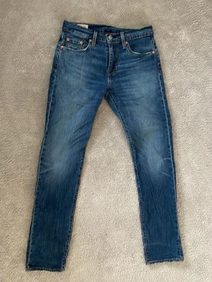 Ljusblåa Levis 502 jeans - Ett par slim fit jeans i storlek W27 L32 av märket Levis. Har bara använt dom några få gånger då de satt rätt så dåligt på mig, den bruna lappen i bak är dock lite urtvättad så att man inte ser siffrorna så bra. Jeansen passar som bäst på dig som har långa ben, beror ju också på hur du vill ha dina jeans.