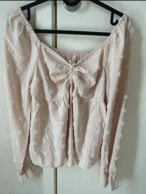 Ljusrosa blus - Supersöt ljusrosa offshoulder blus med långa ärmar och små broderade prickar över hela tyget. Framtill finns en dekorativ rosett och rynkdetalj. Knappt använd 