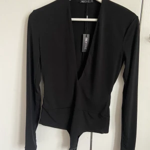 Svart body med djup vringning - Säljer denna jättesnygga oanvända body från Nelly med prislapp kvar och därmed aldrig använd. Finns inte längre kvar på hemsidan. Köpare står för frakten☺️