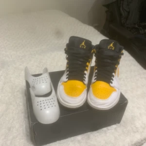 Air jordan 1 mid, WHITE/UNIVERSITY/GOLD/BLACK - Storlek 41, bra skick lite använda inte smutsiga alls och knappt creasade, ny pris 1799 kr säljer dem för 900, creasae skydd ingår!