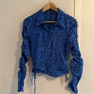 Zara tröja  - Blå långärmad tröja med blommigt mönster på. Tröjan är för liten på mig och den är knappt använd. Den är i gott skick. Längst ner på tröjan finns snören så att man kan dra åt tröjan ifall man nu vill det. 