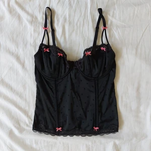 Korsett topp (designer)  - Designer: Betsey Johnson. En vacker svart bustier/korsett topp med många små rosa rosetter. Matrialet har stretch och det finns två inställningar i ryggen. Köpt på Humana, men har själv bara använt den någon gång. Varan har inga skador. Alla varor tvättas