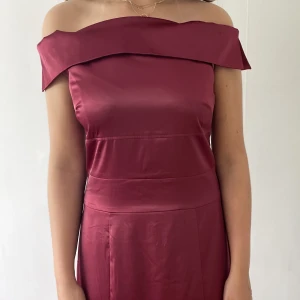 Långklänning till festligheter  - Lång mörkröd silkesklänning som har en offshoulder stil vid axlarna.   Klänningen är använd enbart 1 gång och säljs pga platsbrist. 