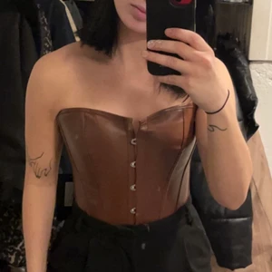 Brun korsett PLT - Brun korsett i läderimitation. Storlek S. Helt oanvänd, lapp kvar. Köpt från Prettty Little thing men slutsåld. Normal i storlek, passar en xs-s och går och anpassa med band baktill för bästa passformen. 