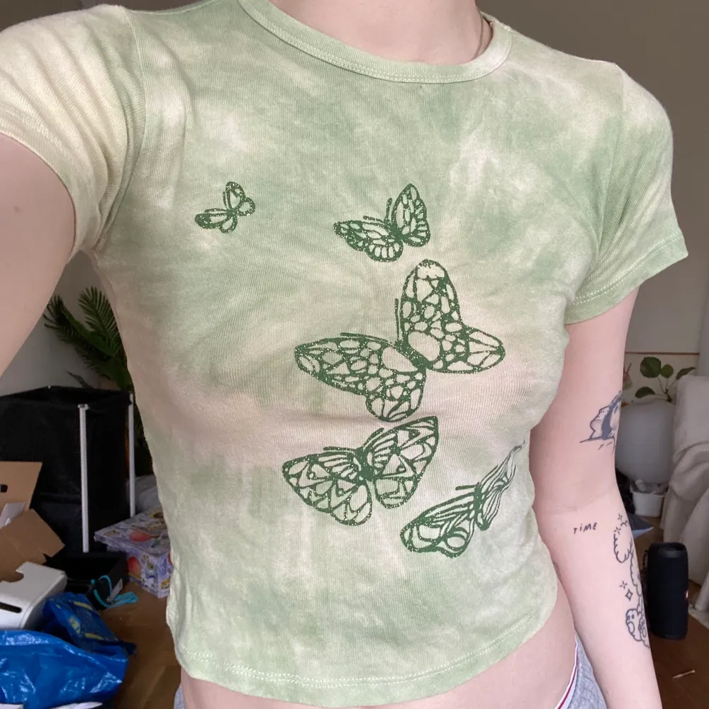 Ljusgrön babytee/croppad t shirt med lätt tie dye-effekt från Urban outfitters. Print med glittriga fjärilar på framsidan, gjord utav 100% bomull dvs supermjuk och något stretchig. Storlek small, 45 cm från axel till nedre kant, 37cm rakt från  armhåla till armhåla. Sitter true to size enligt mig. Fint preloved skick, inga uppenbara defekter. Kan mötas upp på södra sidan av stockholm, annars står köparen för spårbar frakt 66kr. Skriv vid frågor! 💌. T-shirts.