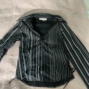 Skjorta - Figursydd skjorta med vita ränder, har knytning i ärmarna, längst ner vid midjan och vid urringningen, så man kan justera hur mycket den ska vara uppknäppt och hur tajt den ska vara. I fint skick!