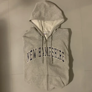 Grå Varsity hoodie - Varisty hoodie i storlek M. Med texten ”New Hamshire” på framsidan. Kan posta eller mötas i centrala Sthlm. Kom gärna med frågor eller fler bilder om plagget.