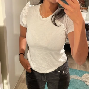 Vit t-shirt - Säljer min trendiga vita t-shirt från Zara, den har lite volanger vid axlarna som är en snygg liten detalj.