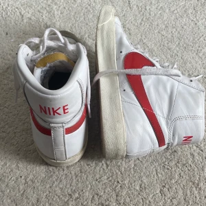 Nike sneakers - Nikeskor modell NSW Nike Blazer mid ’77. Färg vit/röd. Köpta för ca 1,5 år sedan. Använda 5-10 ggr. Fint skick, det som är ”smutsigt” syns på bilderna. Strl US, 8.5 EUR 40. Jag köpte dem för från Nelly de nypris är 1 149 kr. Fler bilder kan skickas. 