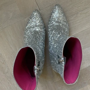 Silverboots 27,5 - Trendriktiga glitter boots från Oscar Tiye (made in Italy) stlk 37,5. Materialet har glitterstruktur. Fodrade m rosa mjukt kalvskinn. Liten taxklack, dragkedja på insidan. Omsulade för att skydda lädersulan. Använd 2 ggr. Nästan nyskick. Dustbag medföljer