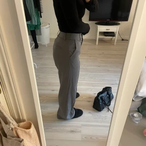 Gråa kostymbyxor - Säljer mina gråa kostymbyxor från nakd. Det är en söm både i fram och bak samt en slits längst ned vid fötterna i bak på varje sida. Fint skick! Är 167 ca