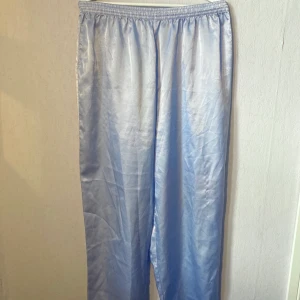 Pyjamasbyxor  - Pyjamasbyxor i satin material. Ljusblå, glansig. Skön och bekväm passform. Byxorna är en del av ett set (se skjortan sista bilden, ligger ute på separat annons) Okänt märke. Aldrig använd av mig och plagget är i mycket gott skick.   Paketpris set= 250