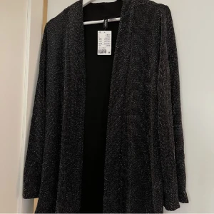 Glitterkavaj strl S - Snygg glitterkavaj från H&M i storlek S. Oanvänd med lappen kvar. Saknar sitt band i midjan men går att använda som en rak kavaj ändå. Har några små lösa trådar på en arm, se bild.  Hör av dig om du har frågor eller vill veta mer. Gott begagnat skick!