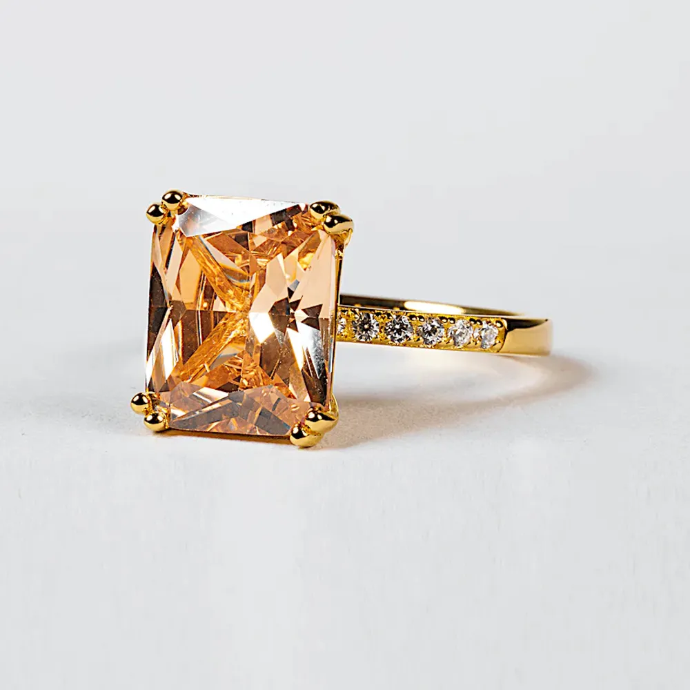 CLÉMENTINE RING från Safira, 18K GOLD PLATED  ”Ringen Clémentine är designad med en stor fyrkantig Cubic Zirconia-sten i en lyxig champagnefärgad nyans. Dessutom pryds den av små ofärgade stenar längs sidorna, vilket ger den ett extra lyxigt utseende.”. Accessoarer.