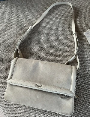 Zadig & Voltaire väska - En snygg Zadig & Voltaire väska i ljus mocka. Inköpt på en Zadig affär i Marseille. Varsamt använd. Många fack inuti, helt rena fack. Kvitto och dustbag följer med. 